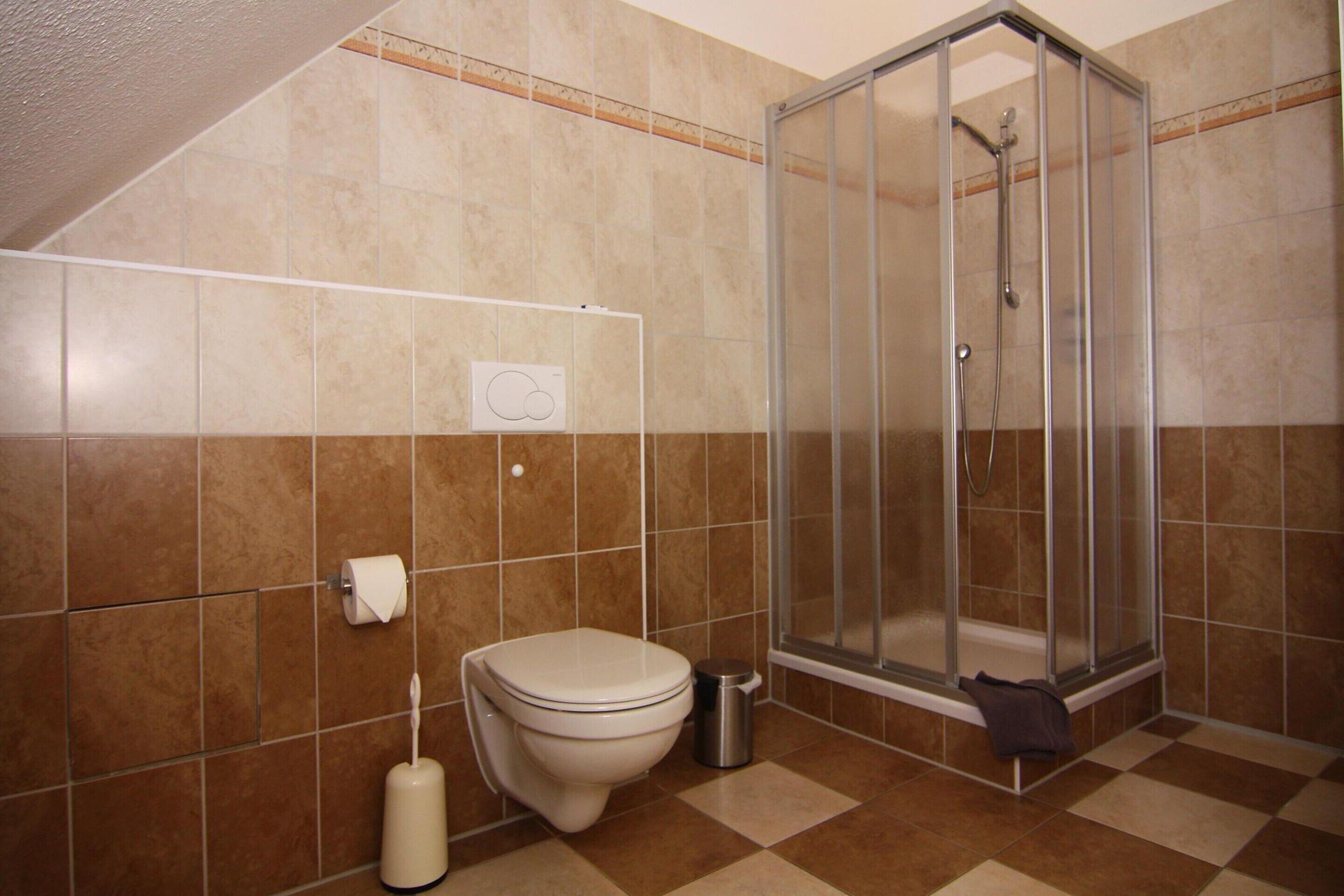 A bathroom with a toilet, a shower, and a tiled floor.