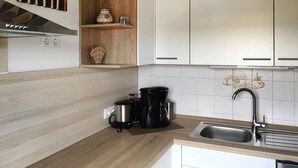 Ett kök med vita skåp, en trähylla, en kaffebryggare och ett handfat.