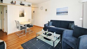 A modern living room with a sofa, a glass coffee table, and a dining area with a table and chairs. - Appartement in Cuxhaven (Cuxhaven)
