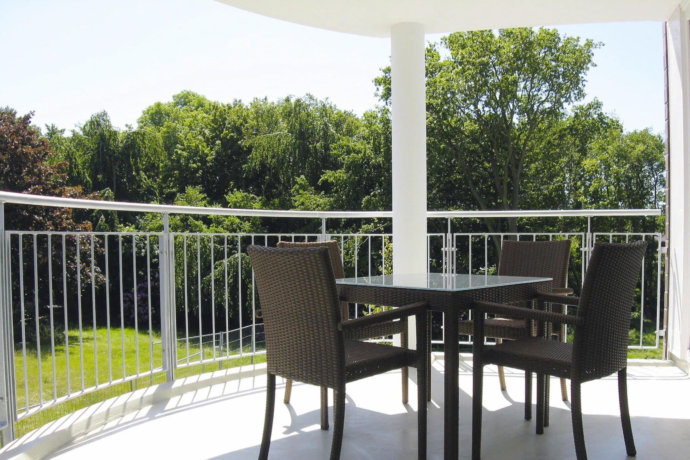 Une terrasse extérieure couverte, avec une table et quatre chaises en osier, entourée d’une balustrade blanche.