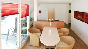 A modern living room with a central table and four chairs, a wooden cabinet, and a red lamp. - Appartement in Cuxhaven (Cuxhaven)