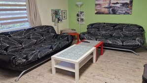 A living room with two black sofas with white leaf patterns, a white coffee table, and a green wall with a landscape painting. - Ferienwohnung in Frankenau (Frankenau)