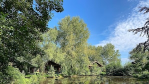 A serene lakeside setting with wooden cabins surrounded by lush greenery and trees. - Ferienhaus in Seenhhe in Hechthausen (Hechthausen)