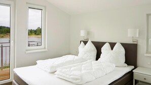 A bedroom with a bed, two bedside lamps, a window, and a view of a body of water. - Ferienhaus in Seenhhe in Hechthausen (Hechthausen)