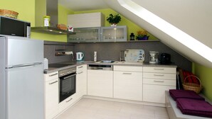 A compact kitchen with a refrigerator, stove, microwave, and sink. There is a small dining area with a bench and a basket. - Appartementhaus am Kiessee, Westerholt (Nenndorf)