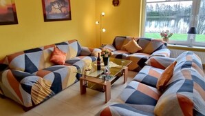 A living room with a sofa set, a glass coffee table, and a window with a view of a lake. - Appartementhaus am Kiessee, Westerholt (Nenndorf)