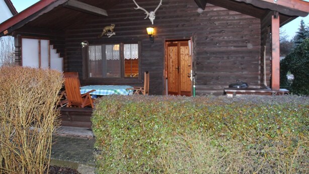 Une cabane rustique en rondins de bois, dotée d’une véranda, d’un lit et d’une table à manger.