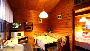 L’intérieur d’un chalet accueillant, avec un décor en bois, une table à manger recouverte d’une nappe à motifs floraux, un banc, un téléviseur et un four à micro-ondes.