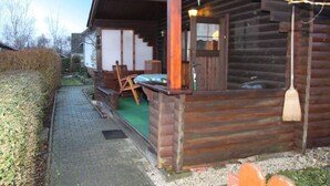Une cabane rustique en rondins de bois, dotée d’un porche, d’un tapis vert et d’un banc en bois.