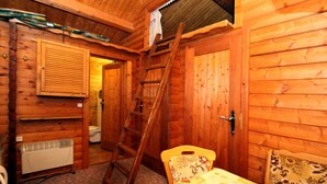 L’intérieur d’une cabane en bois, avec une échelle en bois, un radiateur, une porte en bois et une chaise.