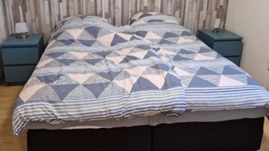 Egy ágy geometriai mintás ágytakaróval, két azonos stílusú éjjeliszekrény és egy fafejtámlával.