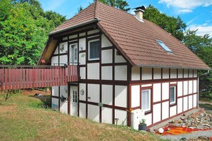 A traditional half-timbered house with a sloped roof, a wooden deck, and a stone foundation. - Ferienwohnung in Frankenau (Frankenau)