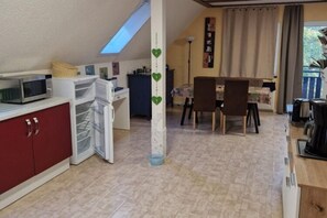 A compact kitchen with a microwave, a refrigerator, and a dining area with a table and chairs. - Ferienwohnung in Frankenau (Frankenau)
