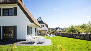 A modern house with a large patio, a stone wall, and a well-maintained lawn. - Ferienhaus, Fuhlendorf (Fuhlendorf)