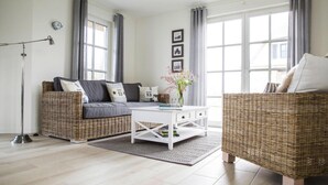 A modern living room with a sofa, a coffee table, and a wicker chair. - Ferienhaus, Fuhlendorf (Fuhlendorf)