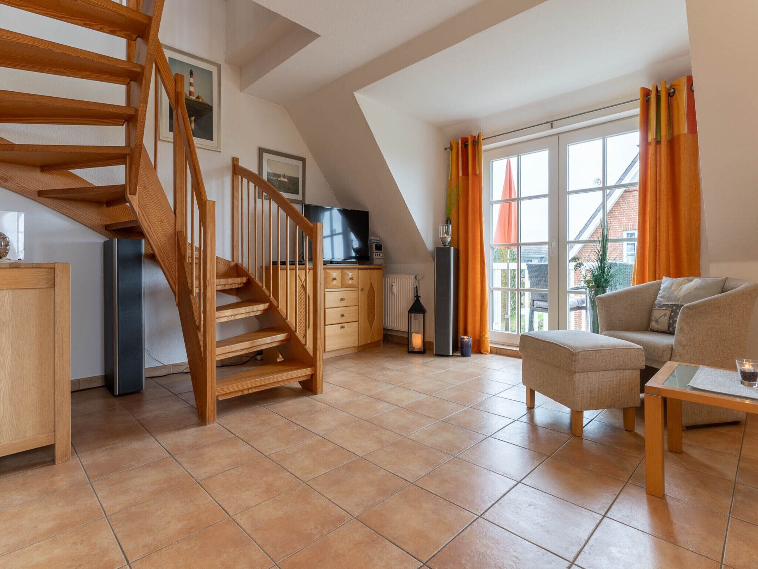 A spacious living area with a wooden staircase, a sofa, a coffee table, and a kitchen area with cabinets and a window.