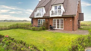 A two-story house with a brick exterior, a balcony, and a large front lawn. - Ferienwohnung, St. Peter-ording (St. Peter-Ording)