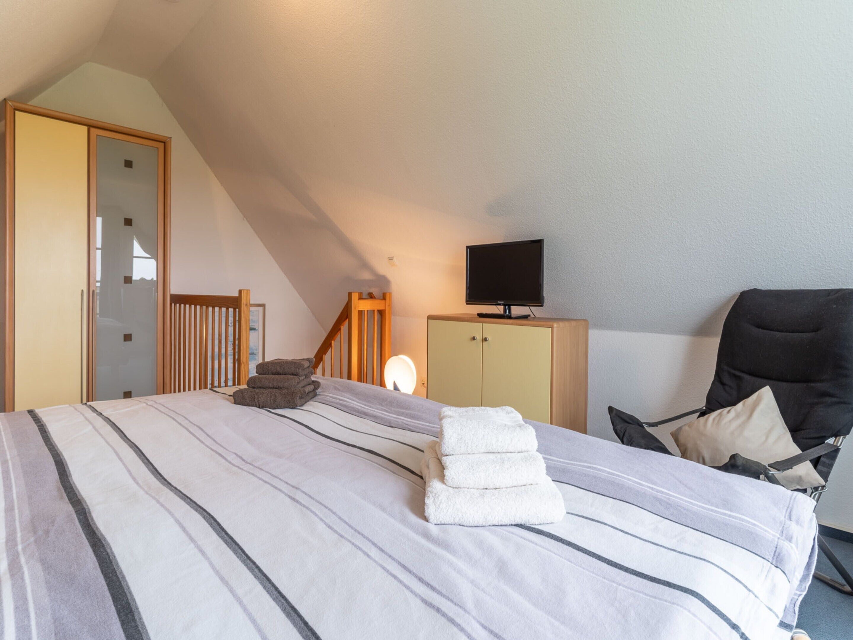 A bedroom with a bed, a television on a cabinet, a chair, and a staircase.
