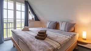 A bedroom with a large bed, a window with curtains, a bedside table with a lamp, and a view of the outdoors. - Ferienwohnung, St. Peter-ording (St. Peter-Ording)