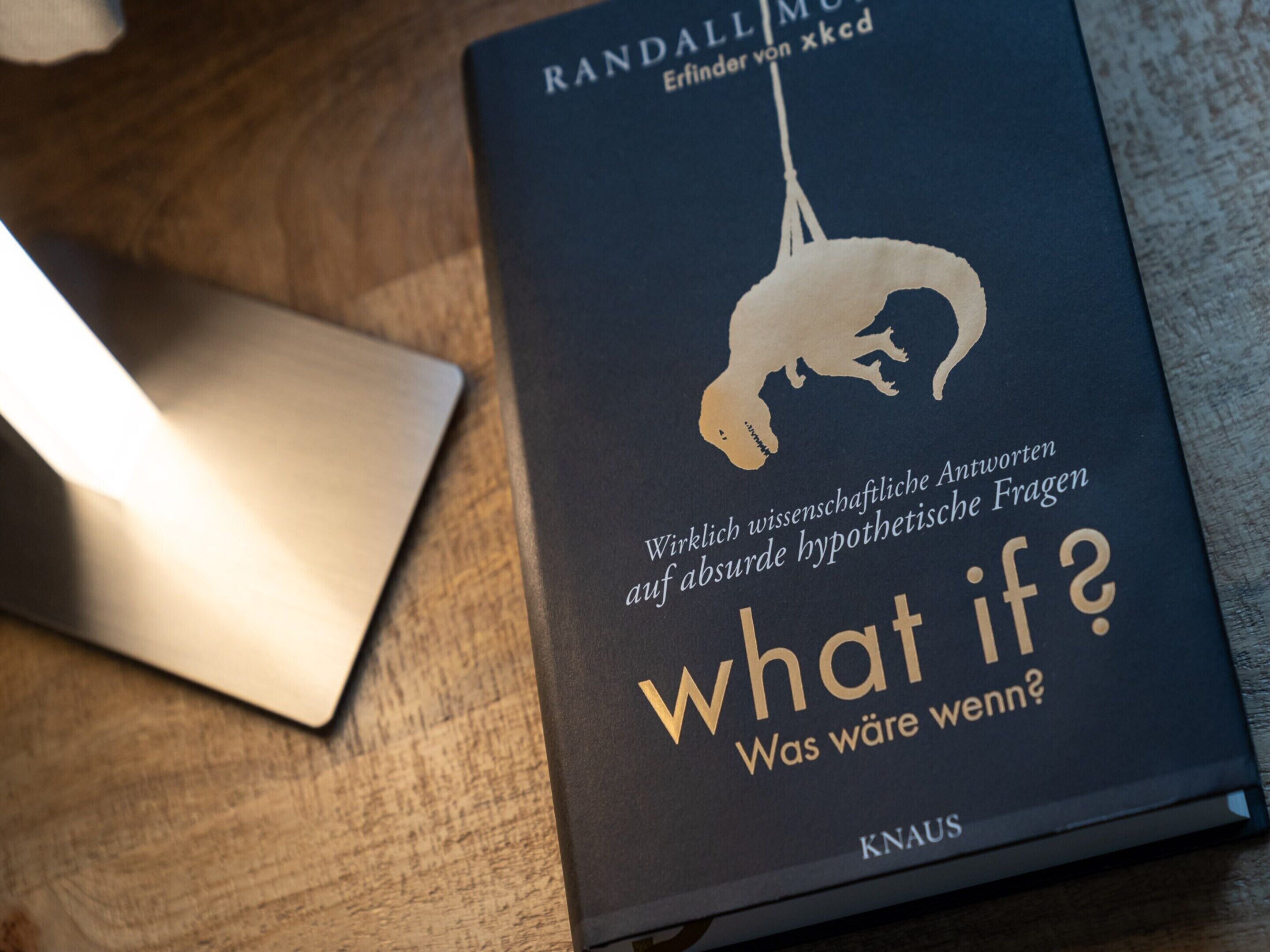 A book titled "What if?" by Randall Munroe on a wooden surface.