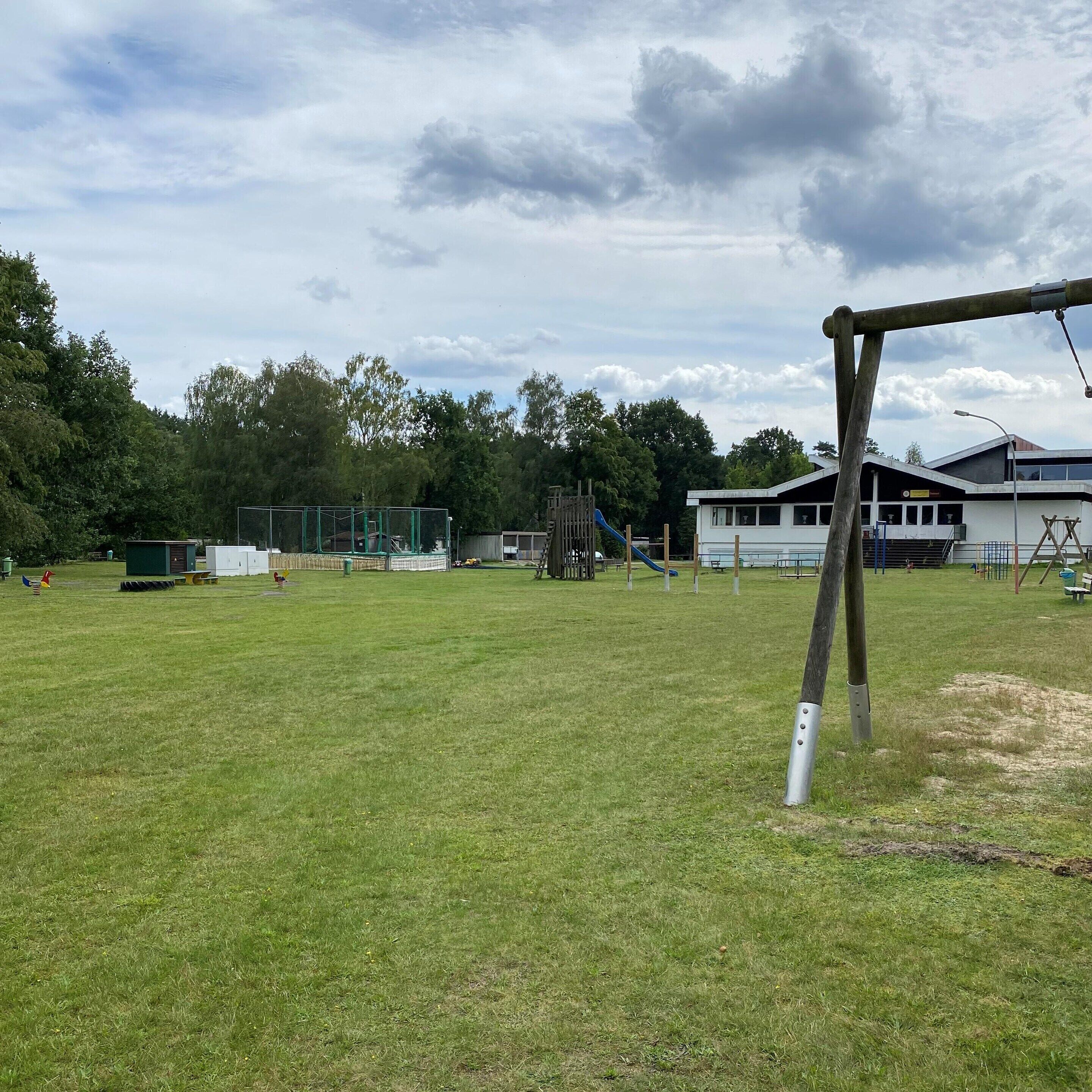 Un campo cubierto de césped con un columpio, juegos infantiles y un edificio con un letrero.