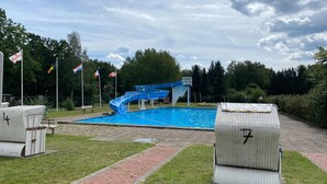 A swimming pool with a blue slide, surrounded by grass and trees. - Gemutliche Ferienwohnung in Fassberg (Faßberg)