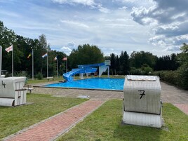 Una piscina con un tobogán azul, rodeada de césped y árboles.
