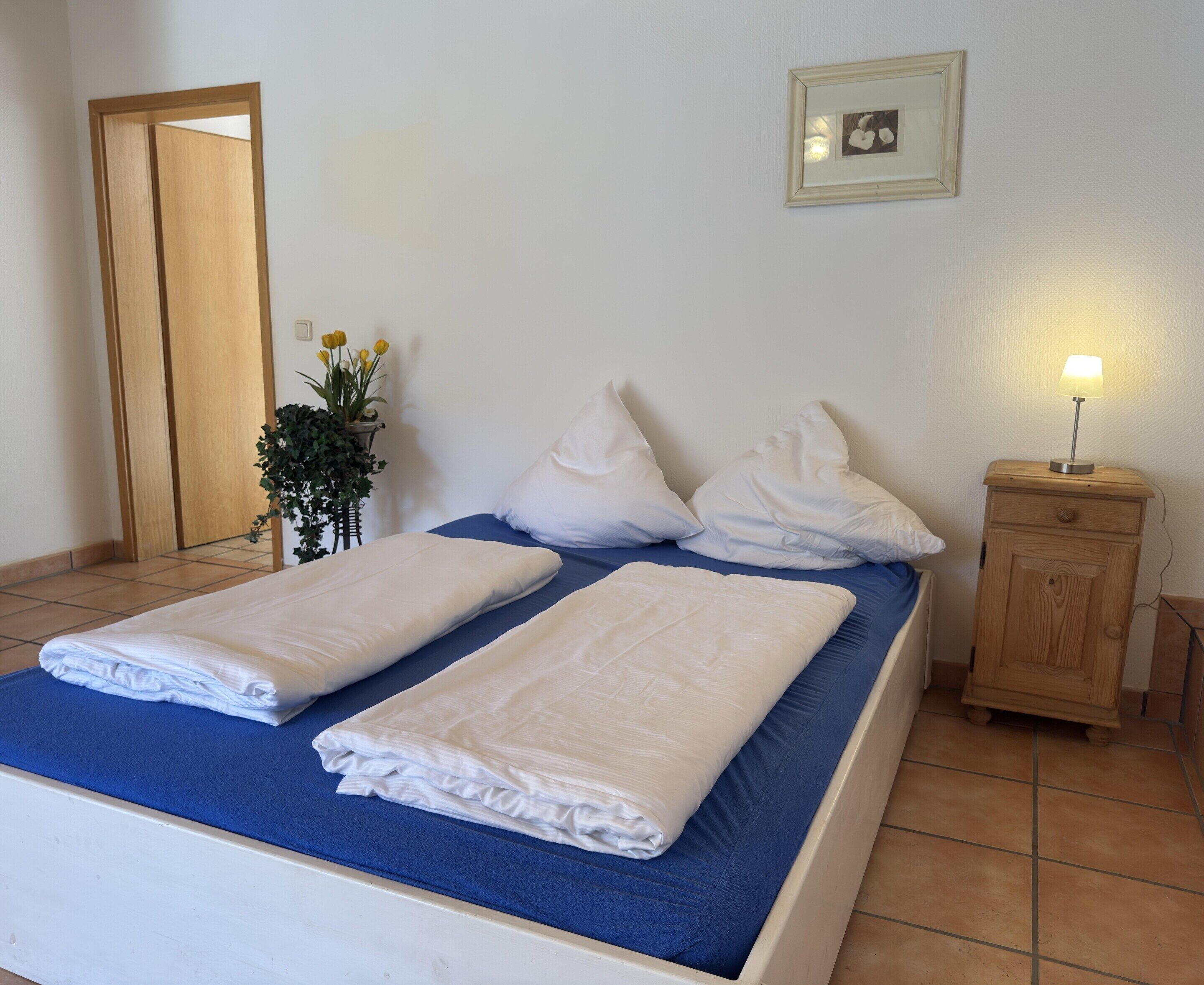 A neatly made bed with white linens, a bedside table with a lamp, and a framed picture on the wall.