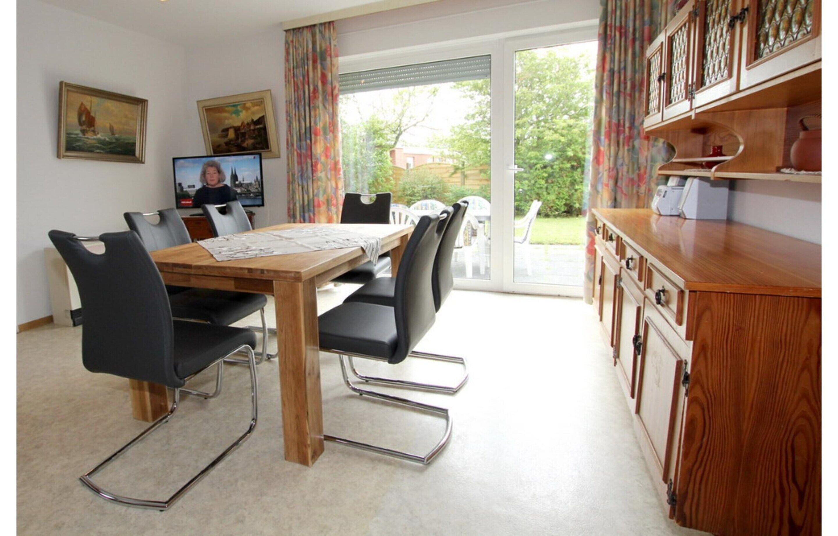 A dining area with a wooden table, black chairs, and a television on the wall.