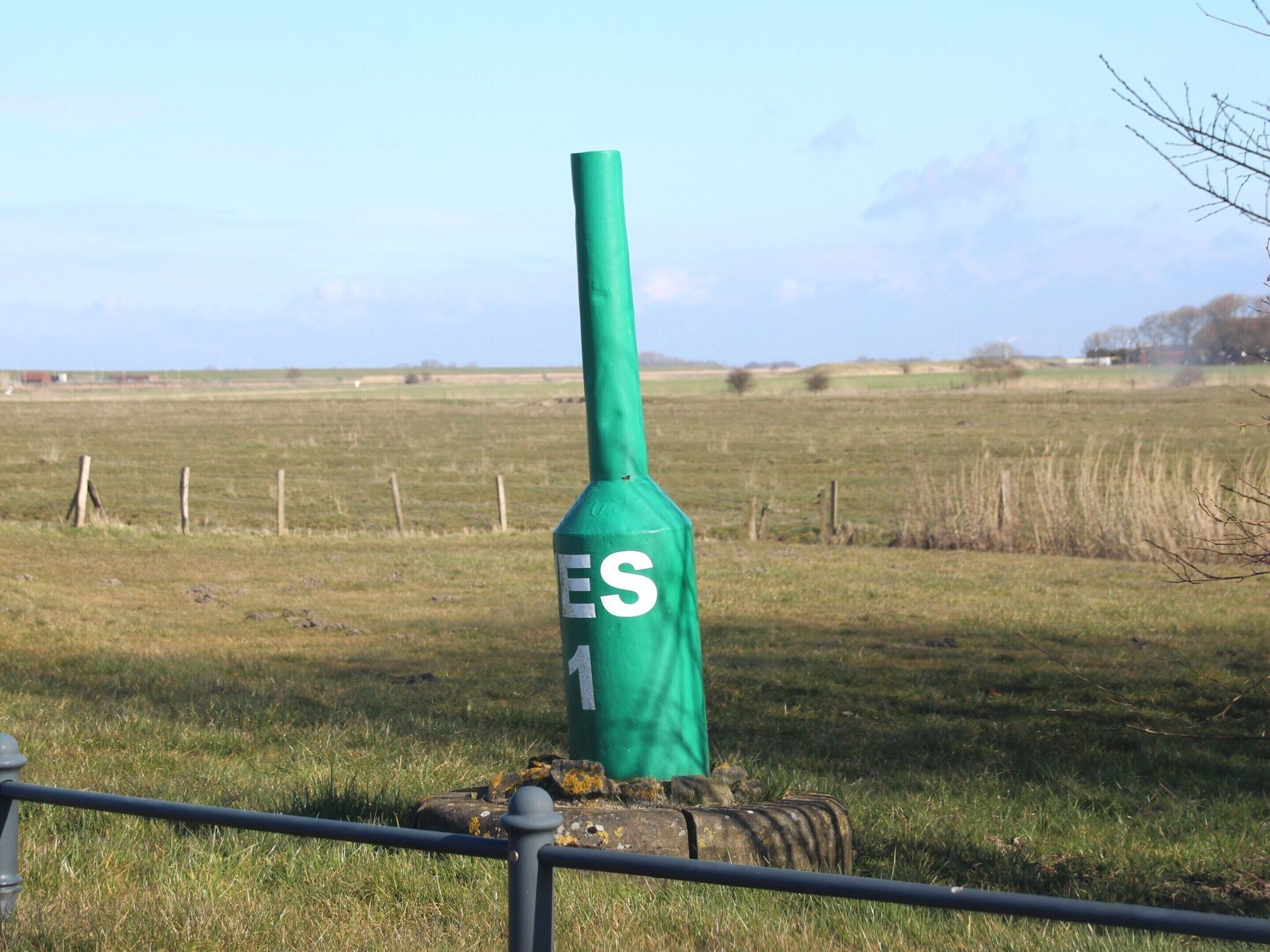 A green pole with the number 1 on it, standing in a grassy field with a fence in the foreground.