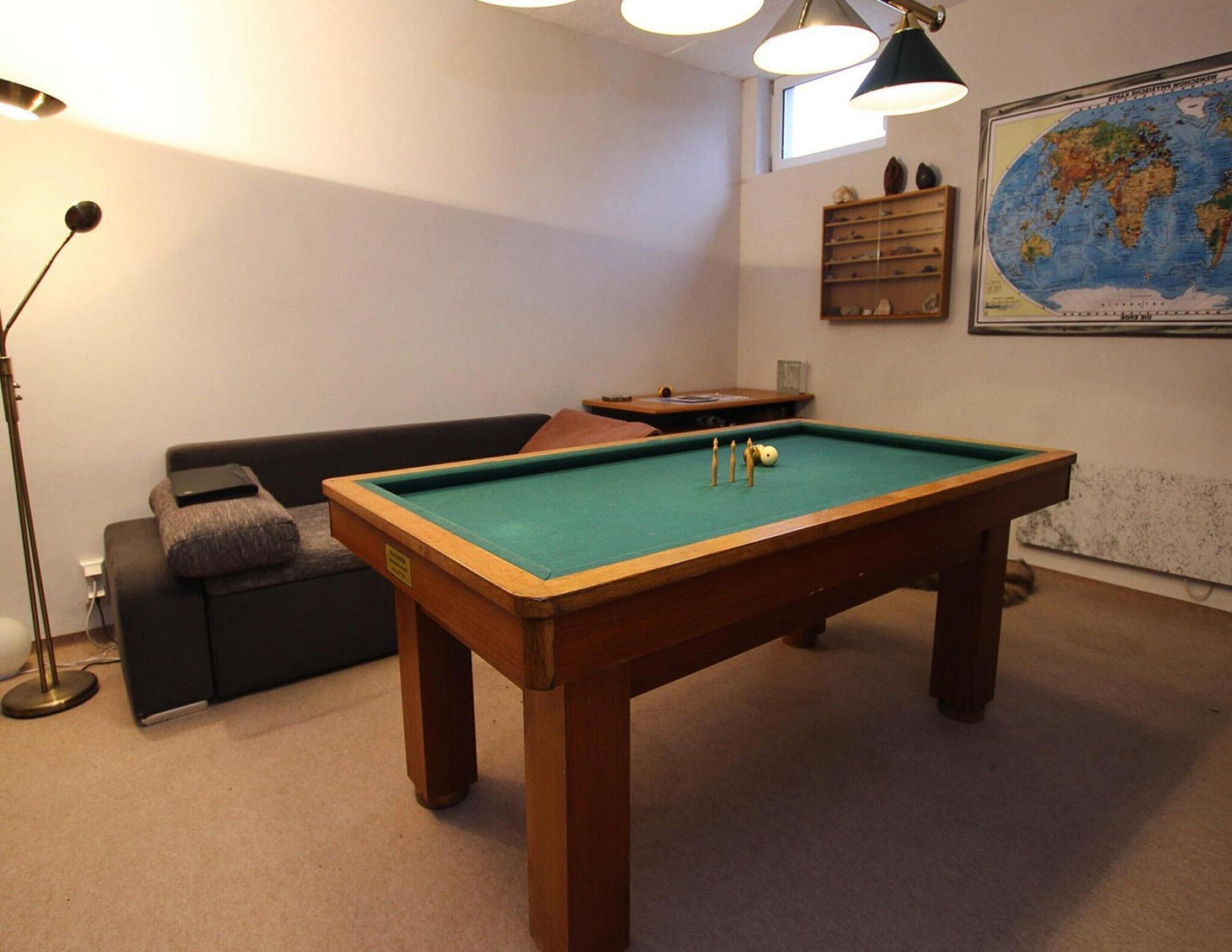 A pool table in a room with a sofa and a lamp.