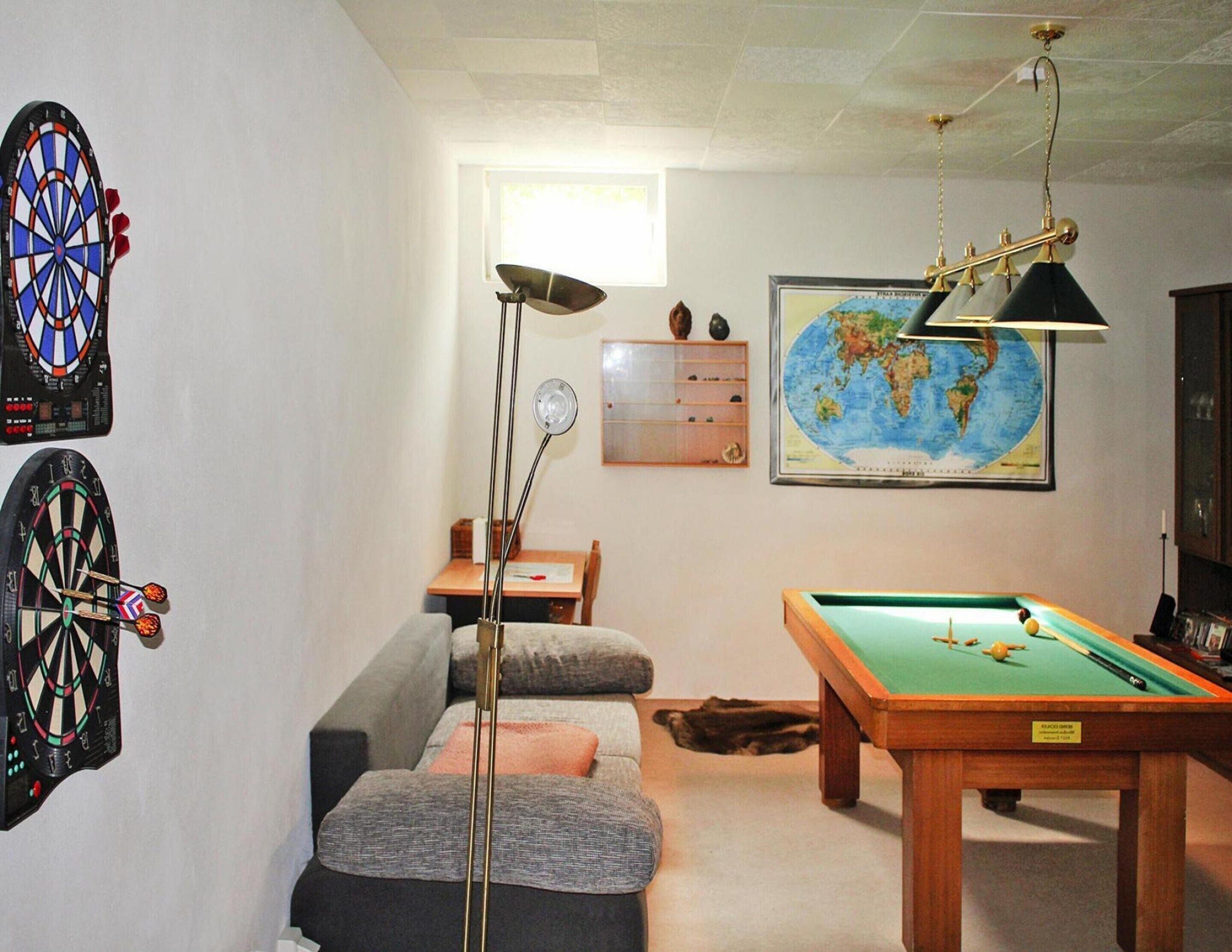 A room with a dartboard, a pool table, a sofa, a lamp, a globe, and a map on the wall.