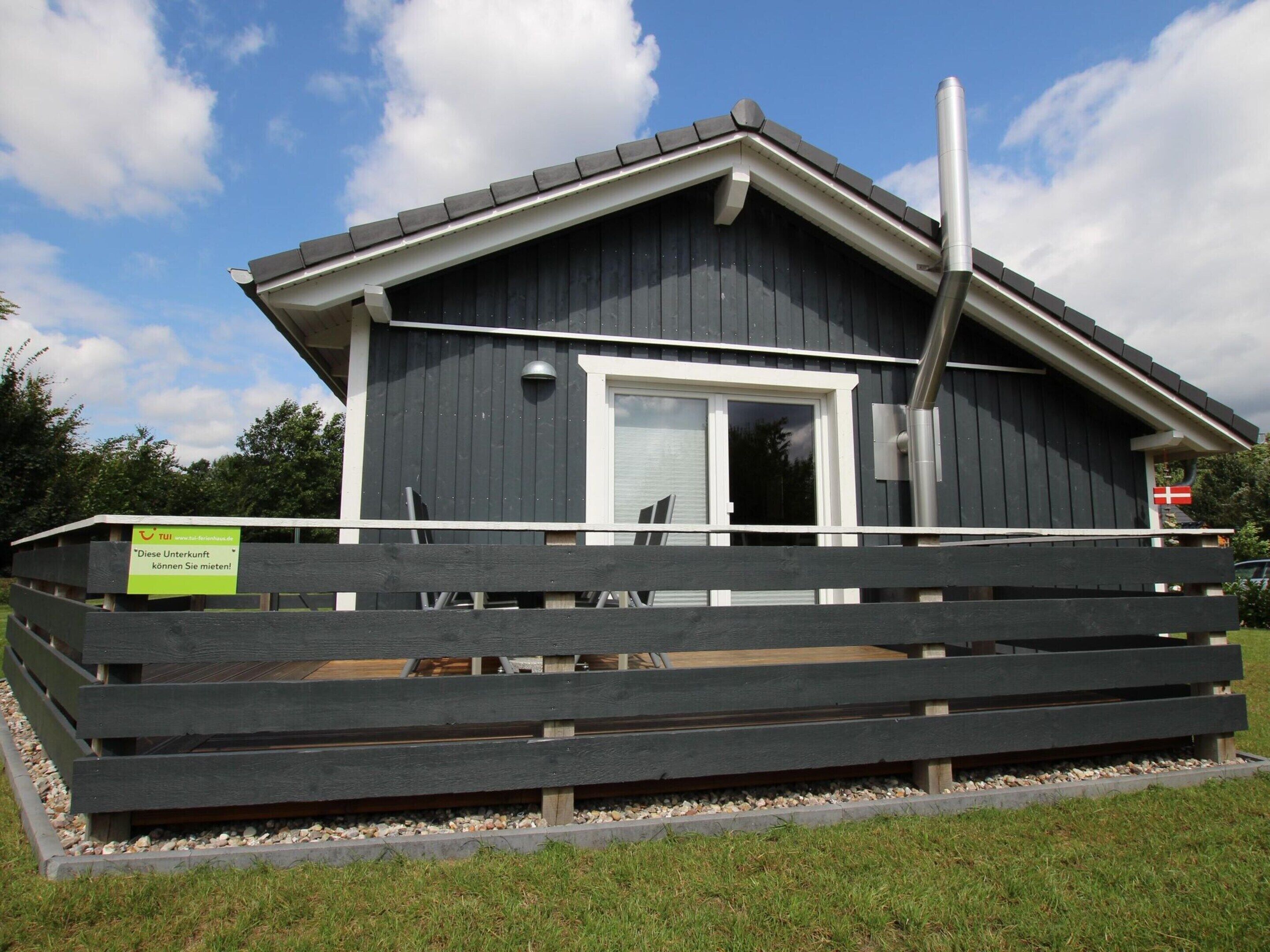 A small, dark wooden building with a white door and windows, surrounded by a wooden fence.