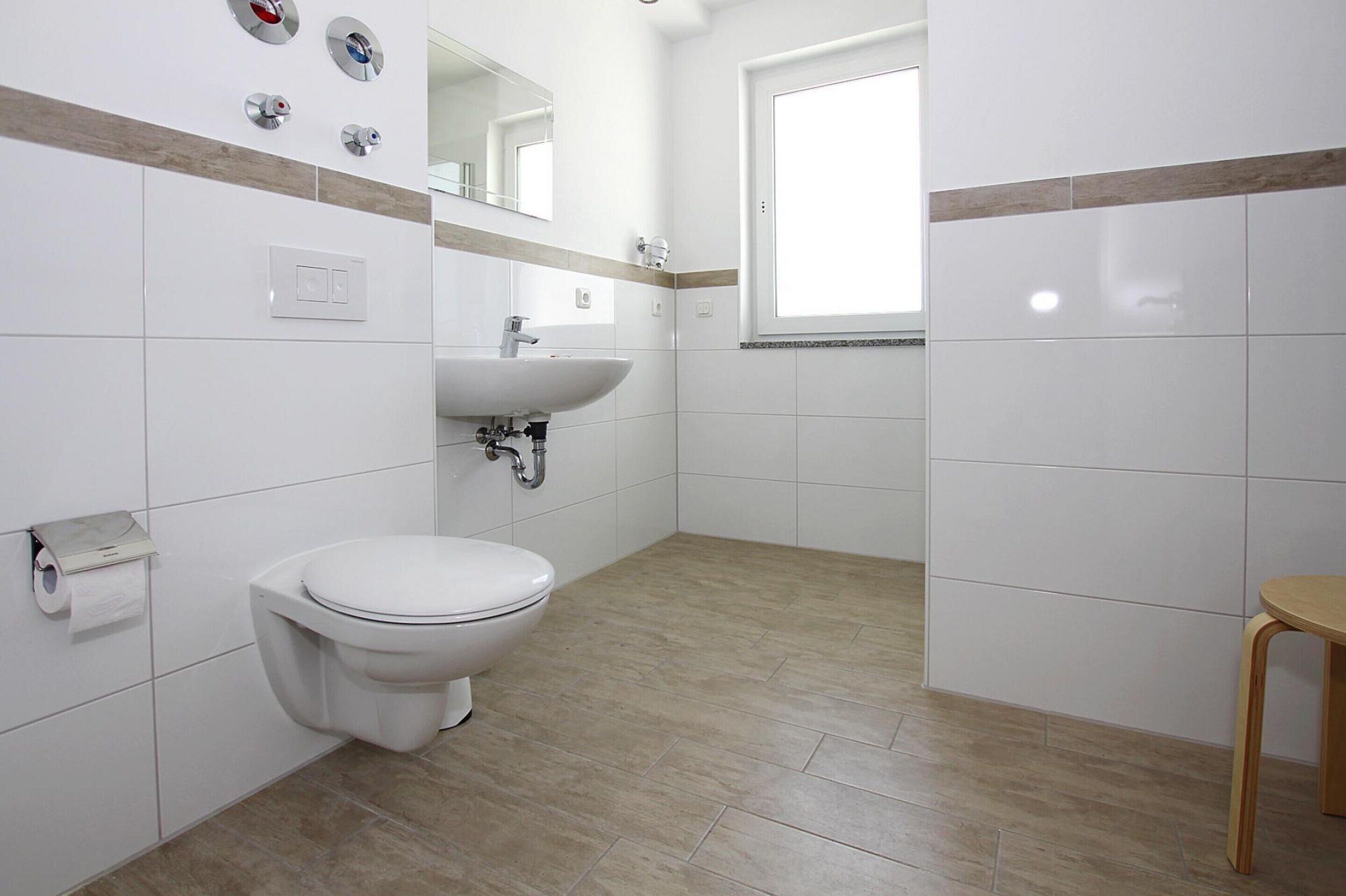 A bathroom with a toilet, sink, mirror, and a window.