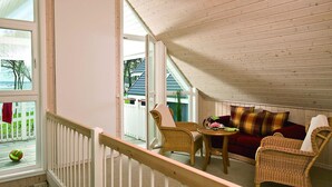 Ein gemütliches Zimmer mit hohen Decken, Holzbalken, Korbmöbeln und Blick auf einen weißen Zaun sowie auf Grünflächen.