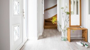 A hallway with white doors, a wooden staircase, a mirror, and a small table with a vase of flowers. - Ferienhaus, Fuhlendorf (Fuhlendorf)
