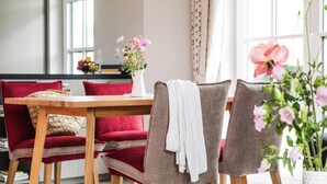 A dining area with a wooden table and red and grey upholstered chairs. There is a vase with flowers on the table, and a clock on the wall. - Ferienhaus, Fuhlendorf (Fuhlendorf)