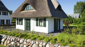 A traditional thatched-roof house with a white exterior, green shutters, and a stone wall in front. - Ferienhaus, Fuhlendorf (Fuhlendorf)