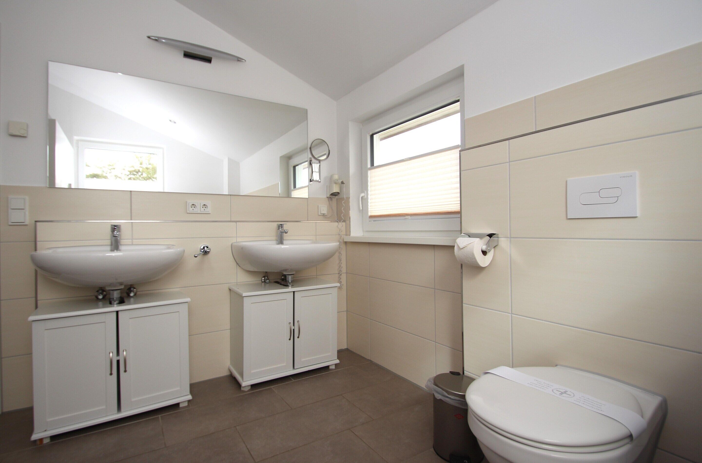 A modern bathroom with two sinks, a toilet, and a window.