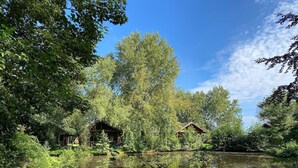Um ambiente tranquilo à beira do lago, com cabanas de madeira rodeadas por vegetação exuberante e árvores.