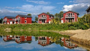 Fileira de casas vermelhas com varandas, refletindo em águas calmas, sob um céu claro.