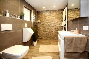 A modern bathroom with a stone wall, a toilet, a sink, and a shower. - Holiday Home Deichperle, Nessmersiel (Dornum)