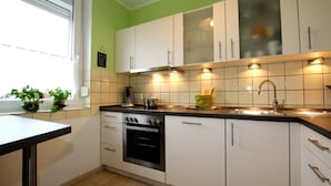 A kitchen with white cabinets, a black countertop, and a window with plants. - Ferienhaus, Dornumersiel (Dornum)