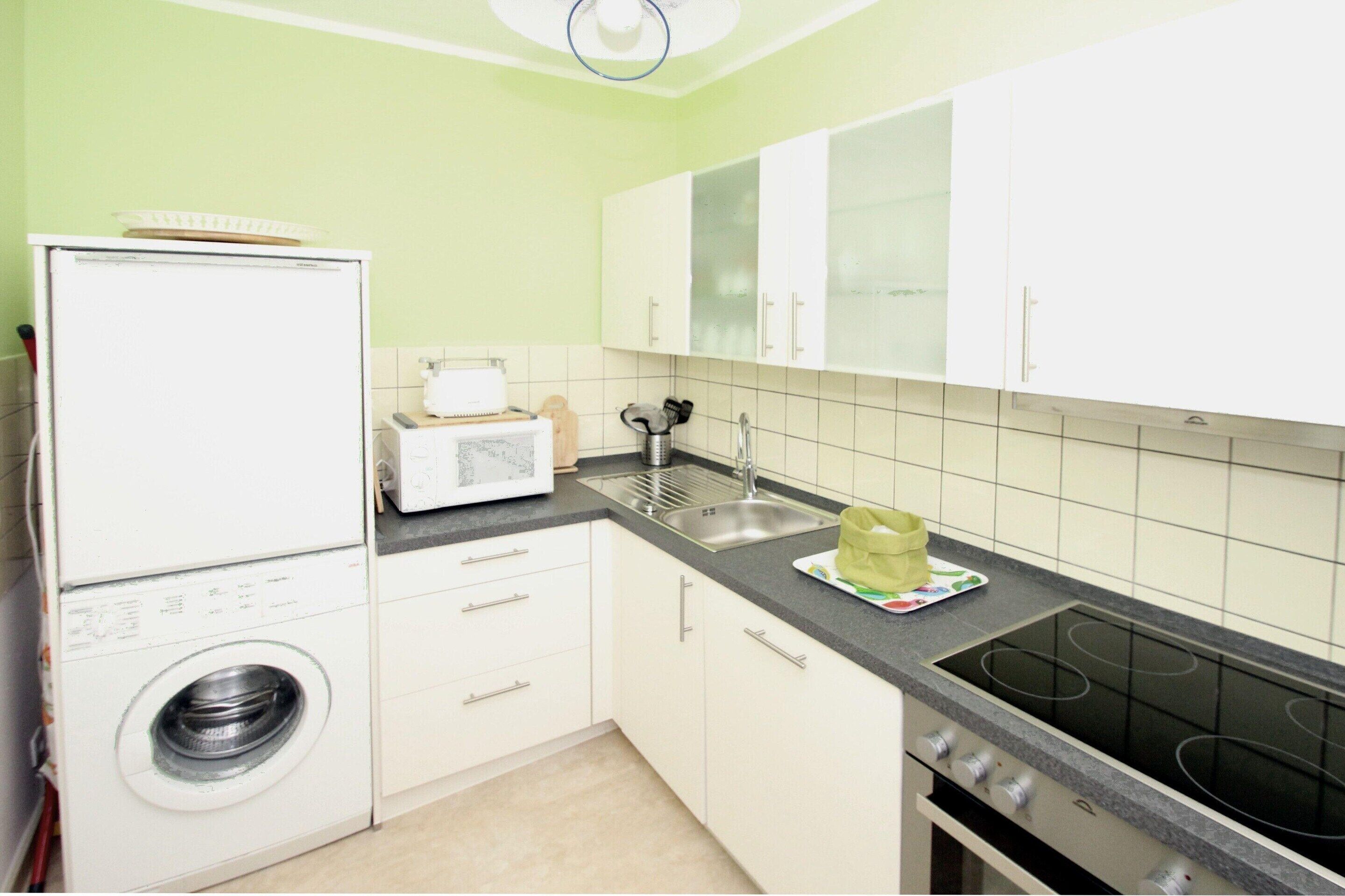 A compact kitchen with a washing machine, a microwave, a sink, and a stove.