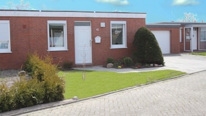 A two-story brick building with numbered doors, a small garden, and a paved driveway. - Ferienhaus, Dornumersiel (Dornum)