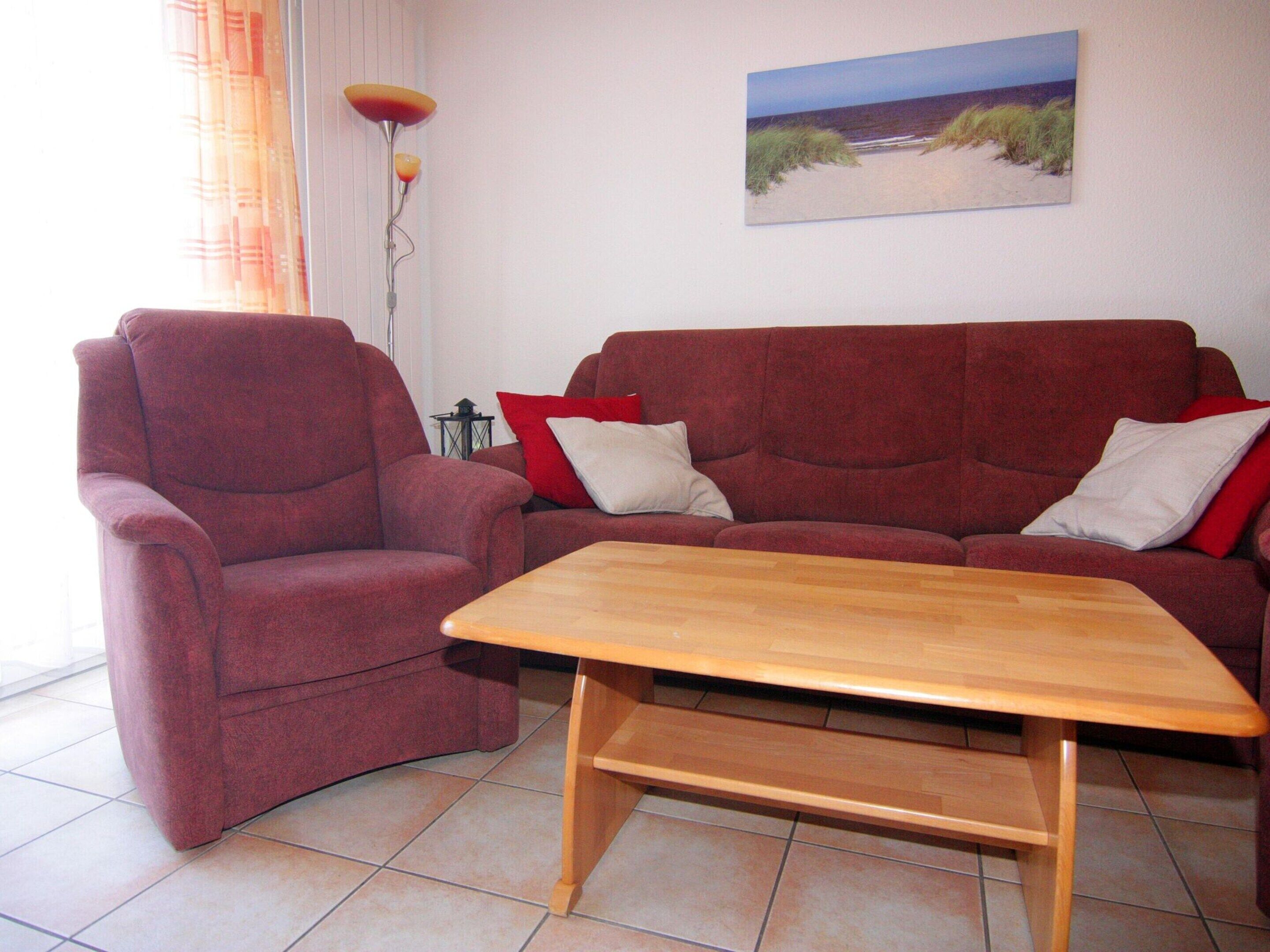 A living room with a red sofa, a wooden coffee table, and a painting of a beach on the wall.