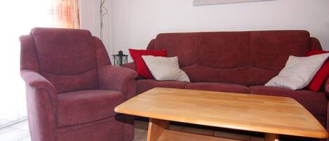 A living room with a red sofa, a wooden coffee table, and a painting of a beach on the wall.