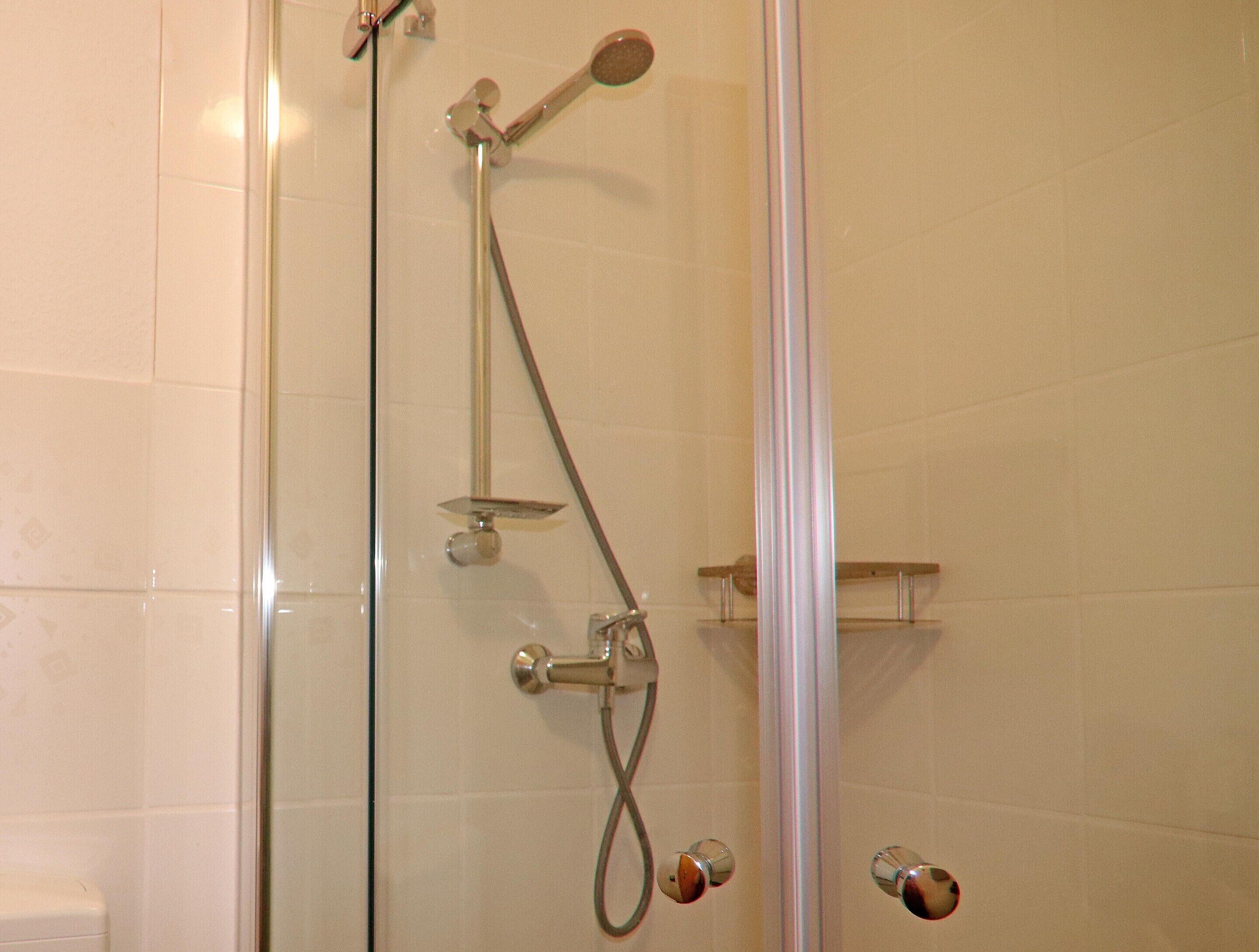 Een douchecabine met glazen wanden, verchroomde details en een handdouche.