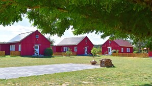 Three red barns with a paved path in front, surrounded by grass and trees. - Ferienwohnung am Oase am Vilzsee (Mirow)