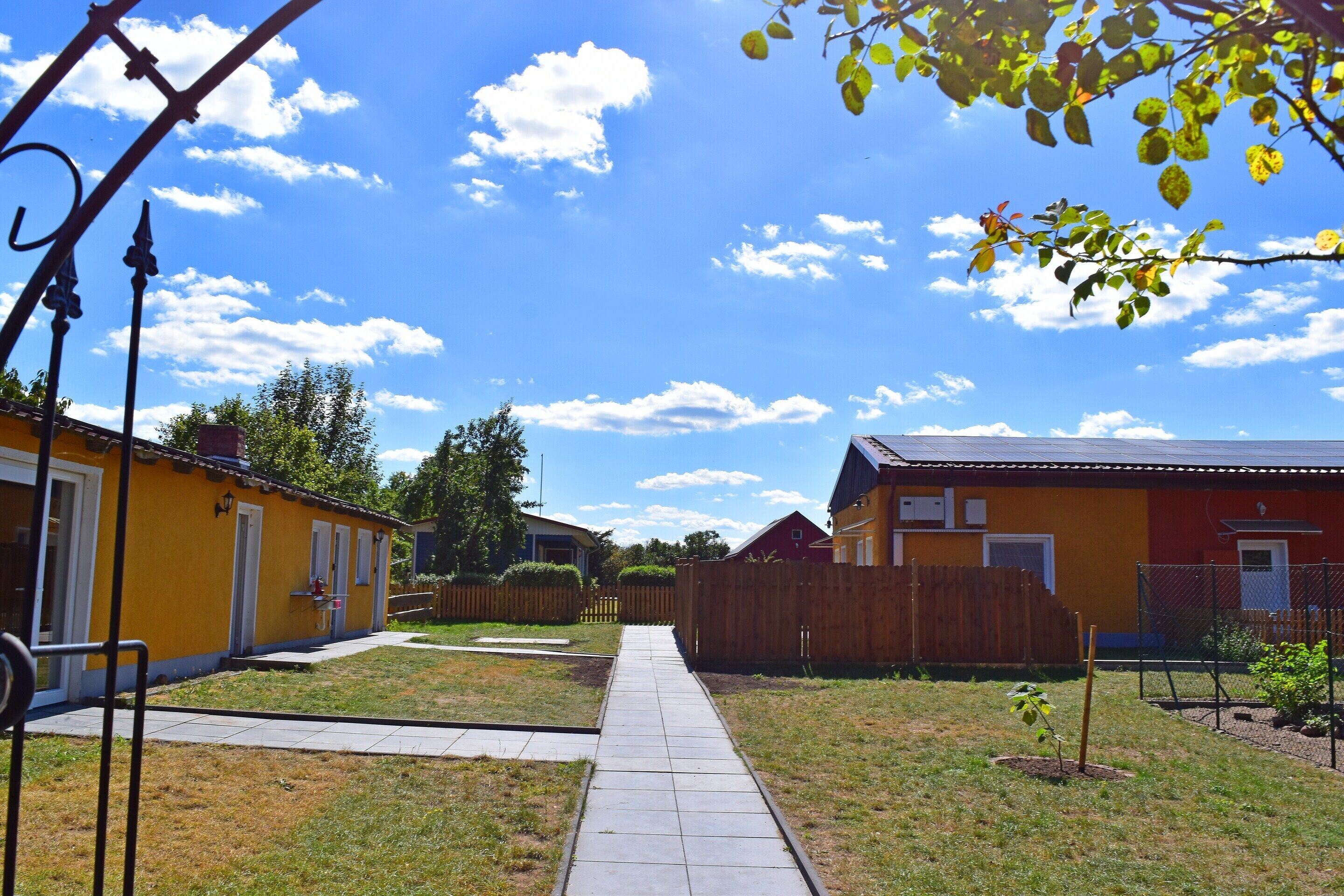 Un quartier résidentiel avec un chemin piétonnier dallé menant aux maisons, le tout entouré de clôtures et de verdure.